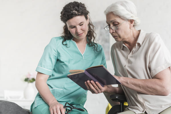 low-angle-view-female-nurse-looking-senior-woman-reading-book